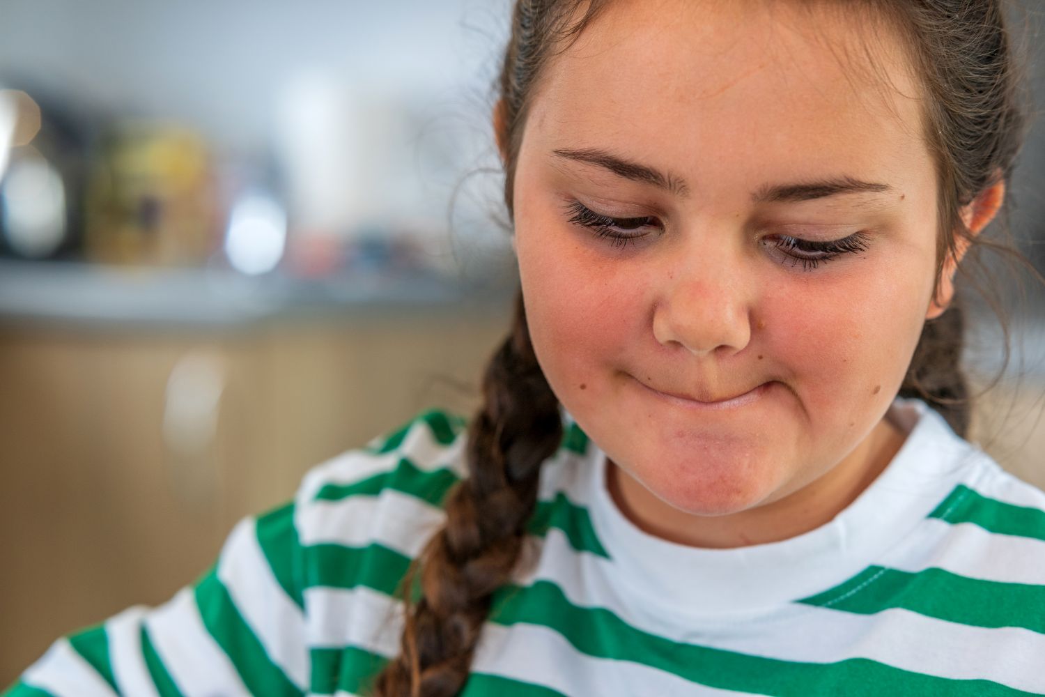 A pensive girl in a green and white striped top, with her dark hair in braided pigtails.