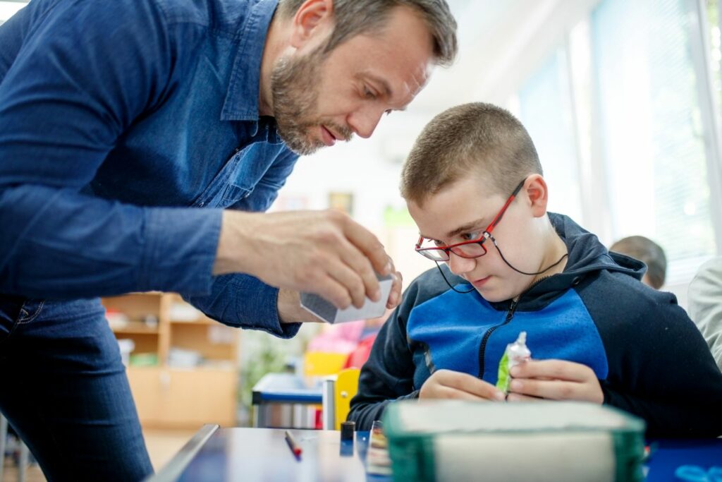A male teacher and young teenage boy work on a technology project together.