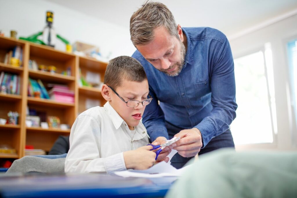 A male teacher and pupil using scissors in the classroom