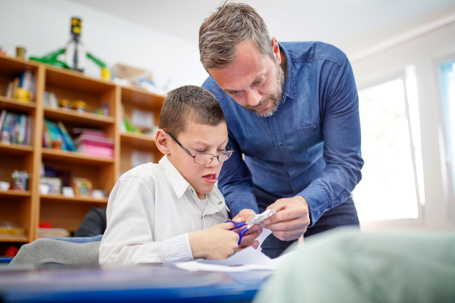 A male teacher and pupil using scissors in the classroom