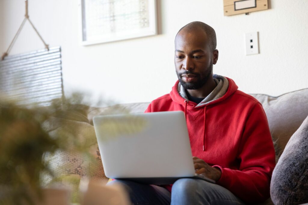 Man sitting in a red jumper with a laptop on his knee.