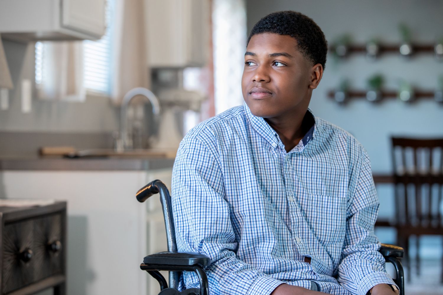 A thoughtful teenage boy in a wheelchair sitting in his kitchen.