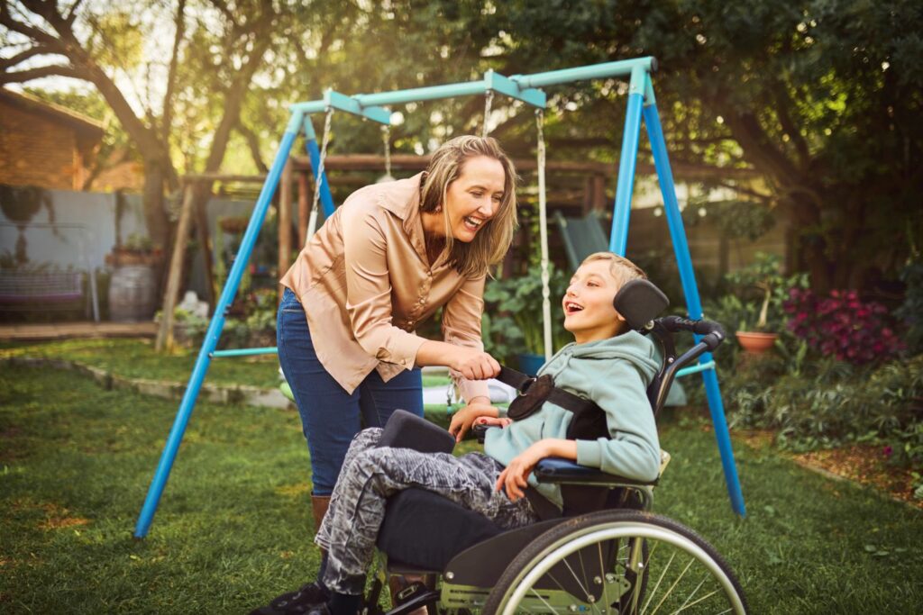 A boy in a wheelchair plays in the garden with his mum.