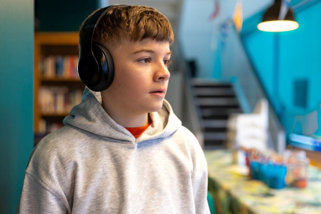 A young teenage boy wearing headphones looks to the side.